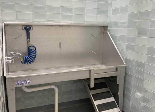 a stainless steel pet wash station with a ramp against a tiled wall