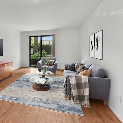 A living room with a grey couch, a coffee table, and a flat screen TV mounted on the wall.