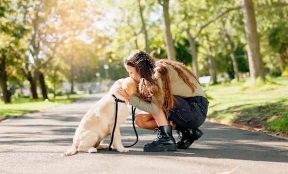 A woman is hugging her dog on a sunny day in the park.