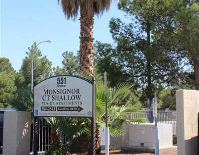 A palm tree stands in front of a sign for Monsignor C. Shallow Senior Apartments.