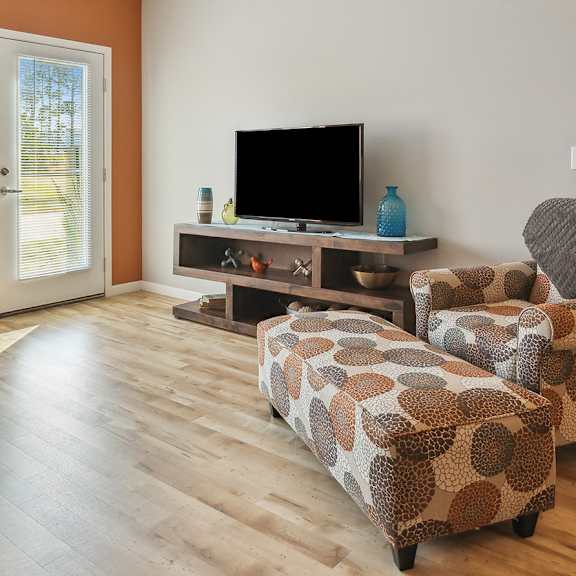 A living room with a grey couch, a brown patterned ottoman, and a flat screen TV.