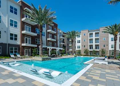 a swimming pool in front of an apartment building with palm trees