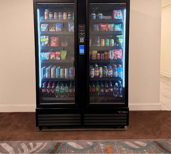 A black double sided fridge with drinks and snacks on both sides.