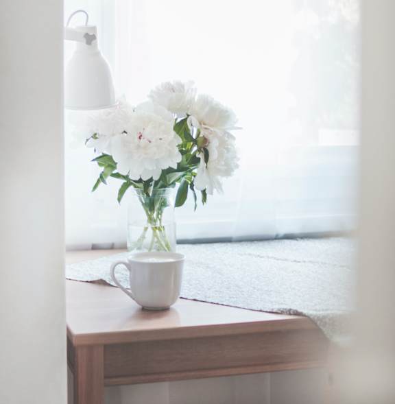 A white couch with a wooden table in front of it and a pair of shoes on the floor.