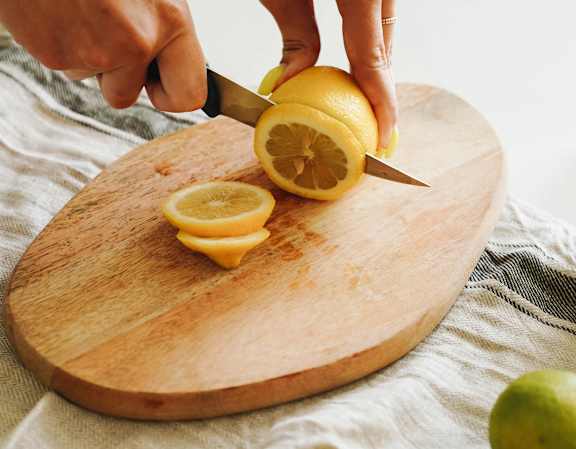 A person cutting a lemon on a wooden cutting board.