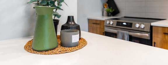 A green vase with a plant sits on a mat in front of a microwave.
