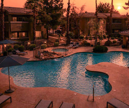 A sunset view of a pool area with palm trees and a building in the background.