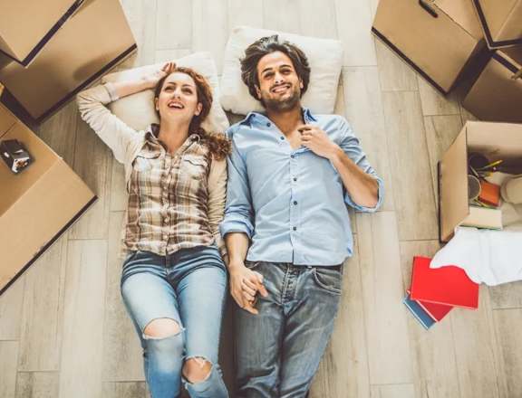 A couple is lying on the floor surrounded by moving boxes.