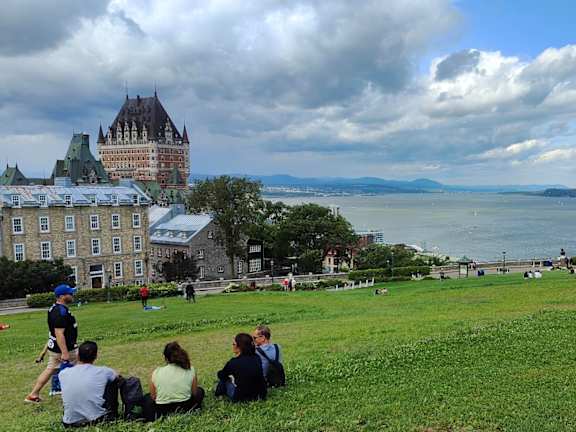 people sitting on a grassy hill overlooking the water and a castle