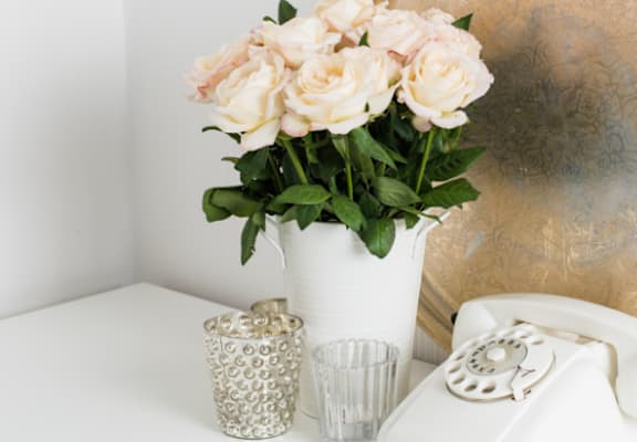 A white telephone sits next to a vase of flowers and two cups on a table.