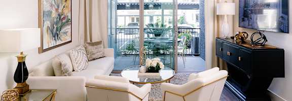 A living room with a white sofa, a black piano, and a glass table with a vase of flowers on it.