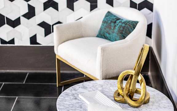 A white chair with a gold design on the back is in front of a black and white geometric wallpaper.