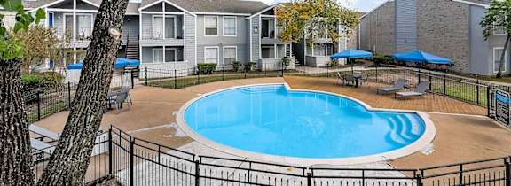 A pool surrounded by a black fence with trees in the foreground.