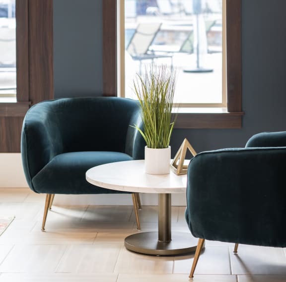 a seating area with two green chairs and a white coffee table with a plant  at The Clearing at ONE28, Olathe, KS