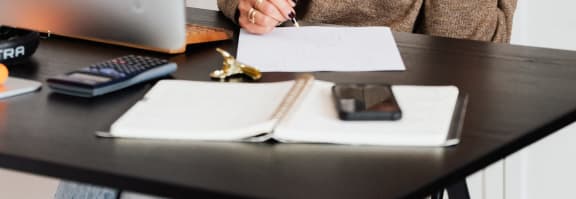 a woman sitting at a desk talking on a cell phone and writing on a paper