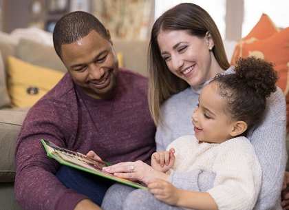 a man and woman sitting on a couch with a child reading a book