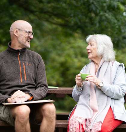 A man and a woman are sitting on a bench in a park.