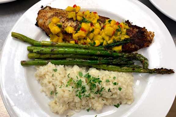 White plate with a piece of grilled fish, a side of mashed potatoes and a side of green asparagus at The Bosk Apartment Homes, Minnesota