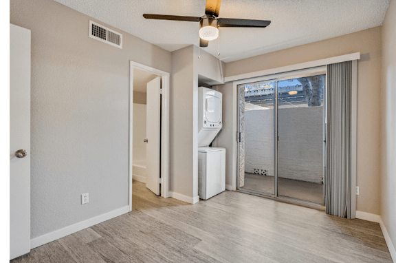A room with a ceiling fan and a window with a view of a parking lot.
