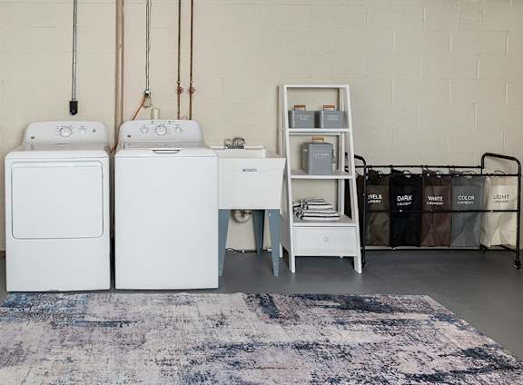A laundry room with a washer and dryer, a small table, and storage bags at Walnut Grove Townhomes* Apartments, Essex, MD
