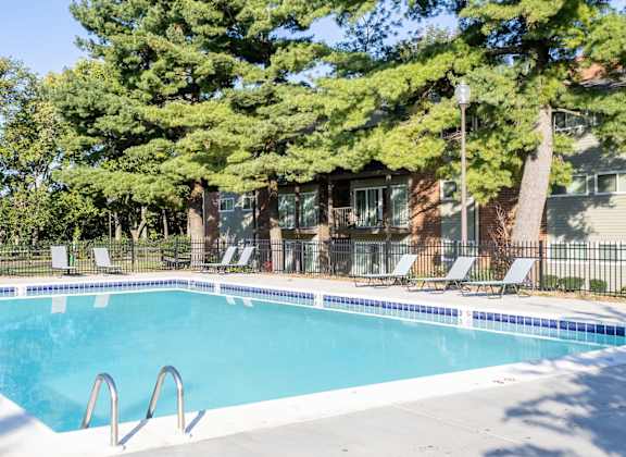 A swimming pool surrounded by trees and chairs.