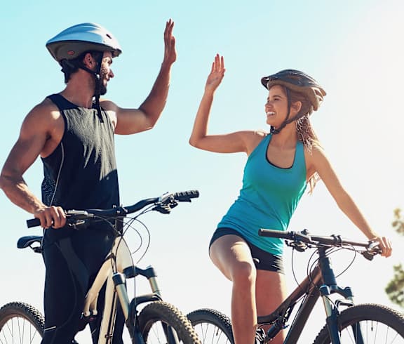A man and a woman are riding bicycles and waving at each other.
