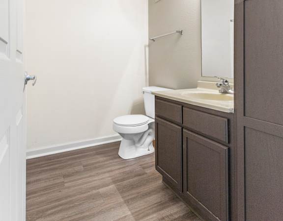 A white toilet sits in a bathroom with brown wood flooring. at Northampton Village Apartments, Indianapolis, Indiana