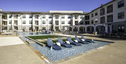 a pool with blue chairs in front of an apartment building