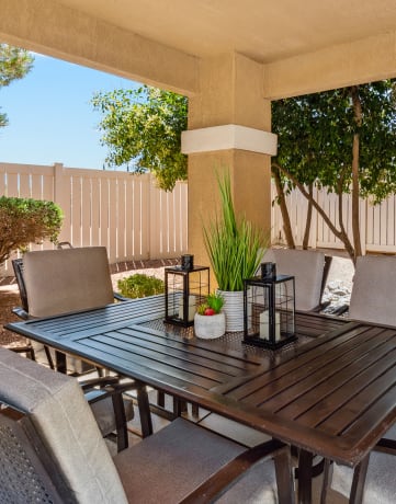 a patio with a wooden table and chairs and a white fence in the background