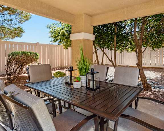 a patio with a wooden table and chairs and a white fence in the background