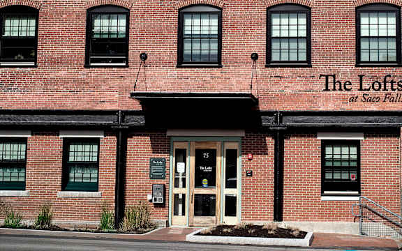 The Lofts at State Falls is a red brick building with multiple windows and a white door.