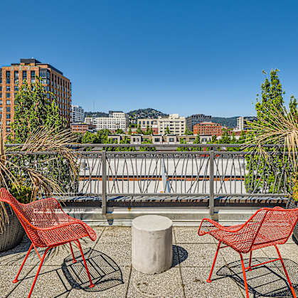 Two red chairs are on a balcony with a view of the city.