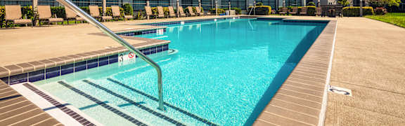 A swimming pool surrounded by lounge chairs and a building in the background.