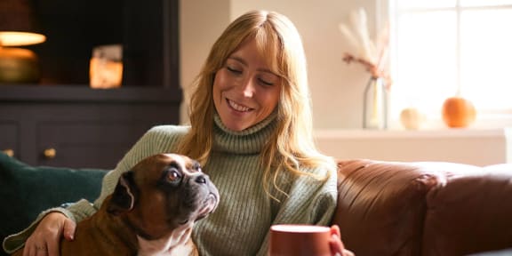 a woman sitting on a couch with her dog and a cup of coffee