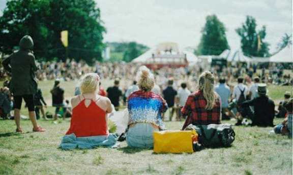 three women sitting on the grass in front of a crowd