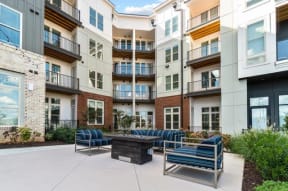 a patio with chairs and a fire pit in front of an apartment building