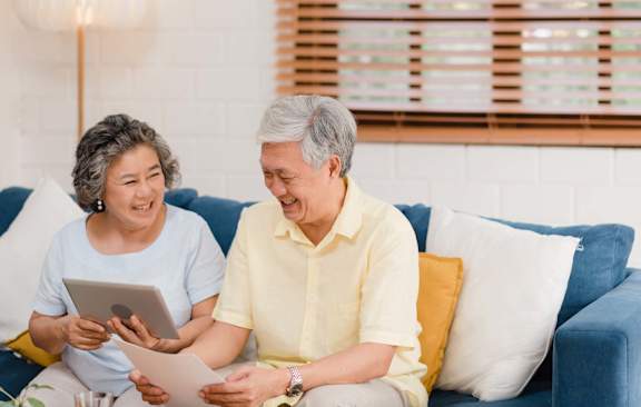 An older couple is sitting on a blue couch, looking at a tablet and smiling.at Cottages at Johnston Commons, Johnston Iowa