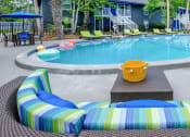 Thumbnail 13 of 23 - Mandarin Bay apartments with pool in Jax, 32257 with lime green loungers and a large green and blue striped patio couch with table.