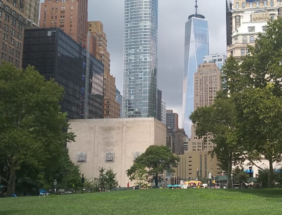 A park with a grassy area and trees in the foreground with a city skyline in the background.
