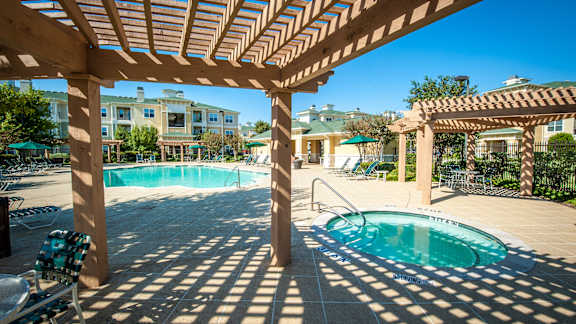 A pool under a wooden pergola with a slide in the background.