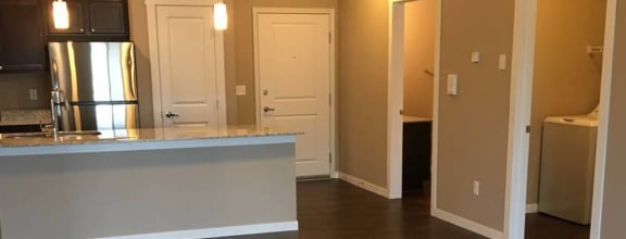 an empty living room with a kitchen in the background