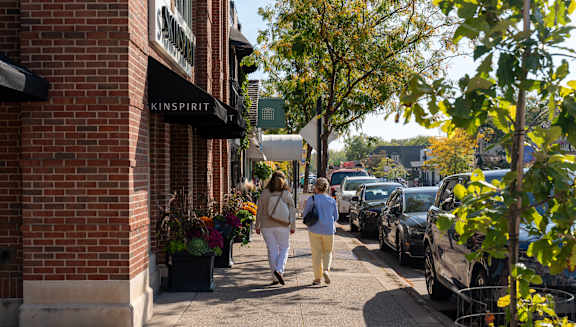 A woman walking down a sidewalk past a store with a sign that says "KINSPIRIT".