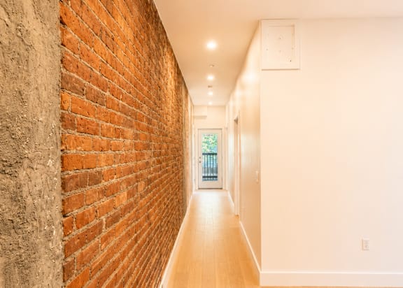 A long hallway with a brick wall on the left and wooden floors.
