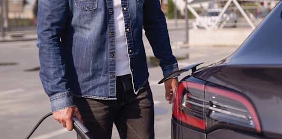 A man in a denim jacket is charging an electric car.