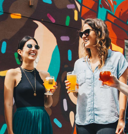 a group of women standing in front of a mural holding drinks
