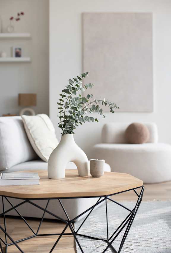 A white vase with greenery sits on a wooden table in a living room.