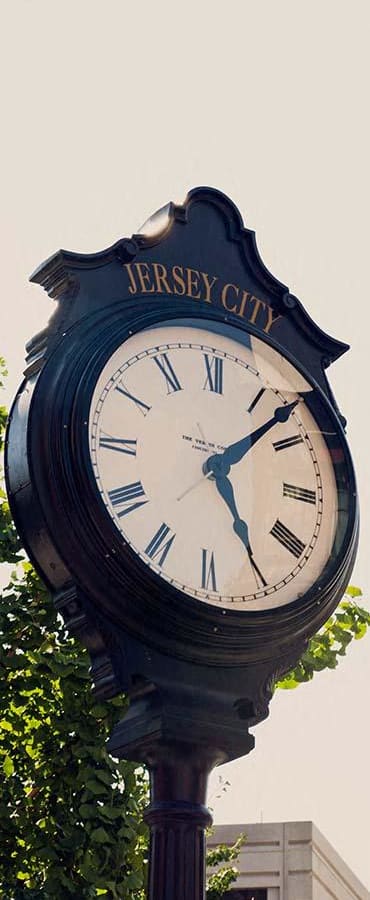 a large clock on a pole in front of a tree at The Enclave, Jersey City, New Jersey