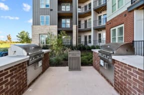 a patio with two grills and an apartment building in the background
