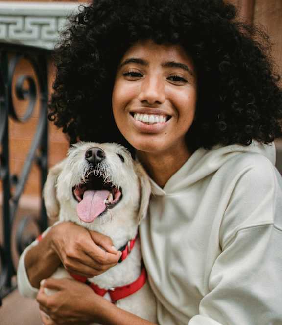 A woman in a white hoodie is holding a white dog with a red collar.