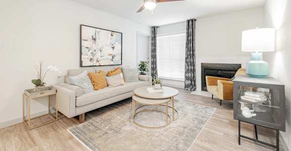 A living room with a grey couch, a coffee table, a side table, a fireplace, and a ceiling fan.